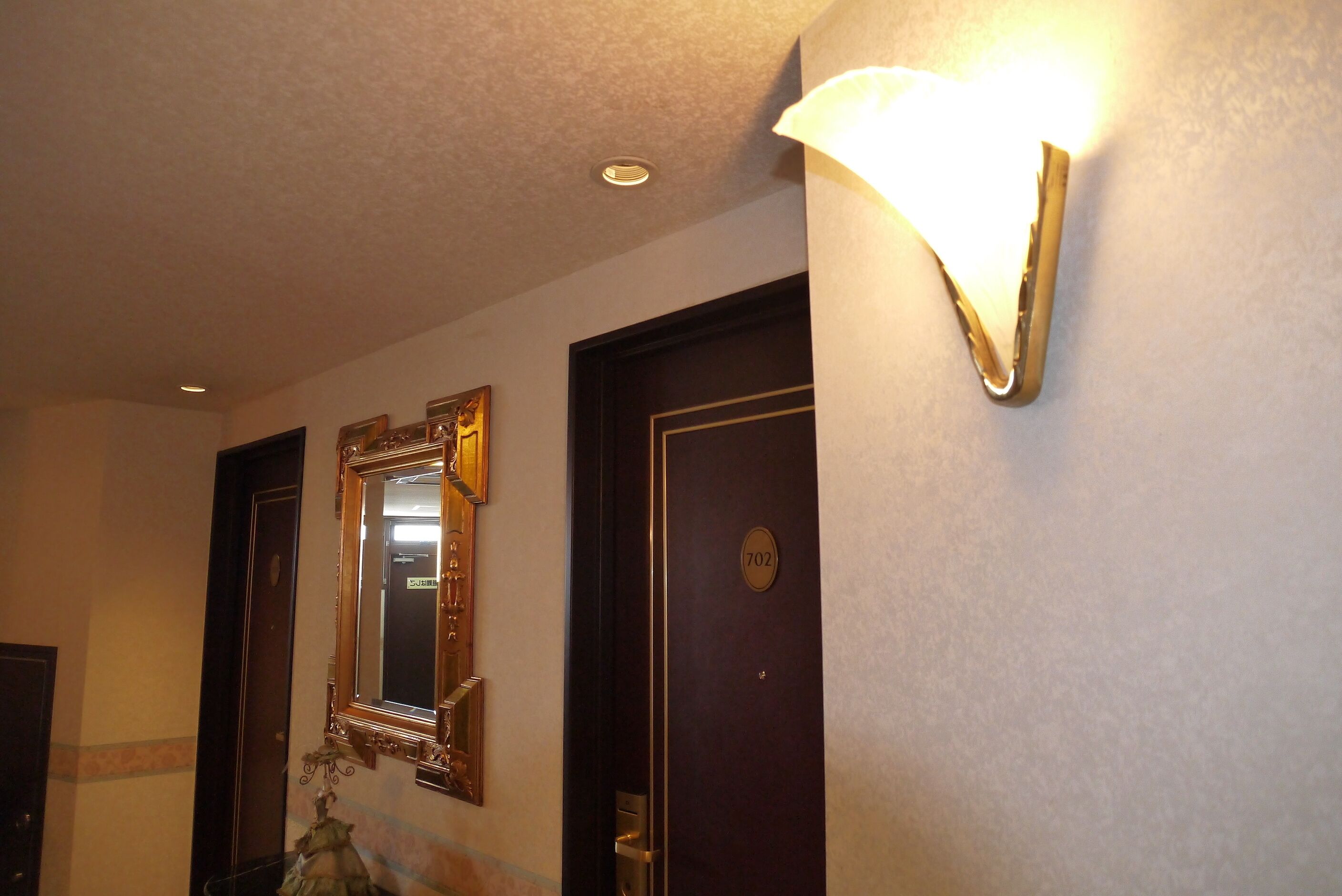 Een hal met een deur met het nummer 702, een spiegel aan de muur en een wandlamp.
