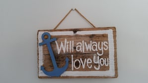 Un letrero de madera rústica con un ancla azul y el texto 'Will always love you'.