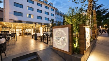 An outdoor dining area with a sign for 'FOODIE-IST' cafe and brasserie, surrounded by a modern building with multiple windows.