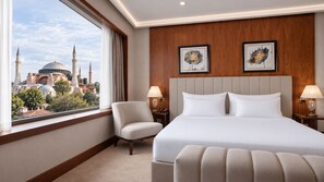 A hotel room with a large bed, two bedside tables, a chair, and a view of a cityscape with a mosque. - Sura Luxury Milion & Spa (Istanbul)