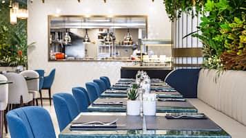 Een restaurant met een lange eettafel, blauwe stoelen en een bar op de achtergrond.