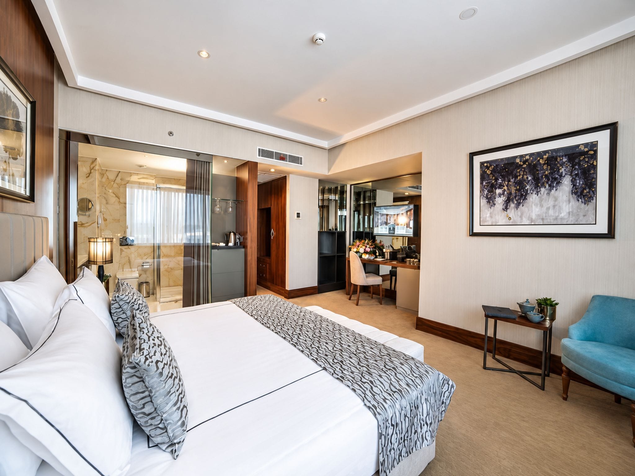 Ein Hotelzimmer mit einem großen Bett, einer Sitzecke mit blauem Sessel, einem Essbereich und einem Badezimmer mit Glasdusche.