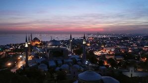 A cityscape at dusk with prominent domed buildings and minarets, likely a historic area with a view of the sea. - Sura Luxury Million & Spa (Istanbul)