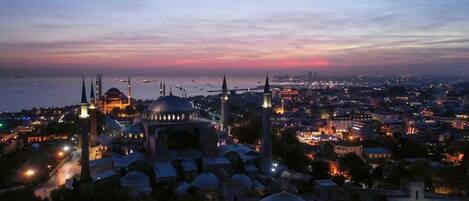 Une vue sur une ville au crépuscule, avec des bâtiments à coupoles et des minarets bien visibles, probablement un quartier historique offrant une vue sur la mer.