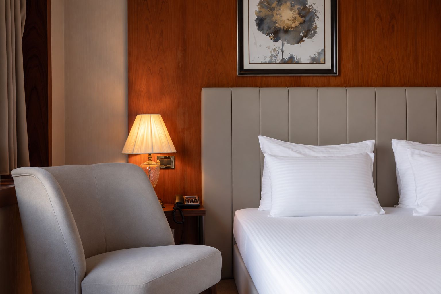 A hotel room with a bed, a chair, a nightstand with a lamp, and a framed picture on the wall.