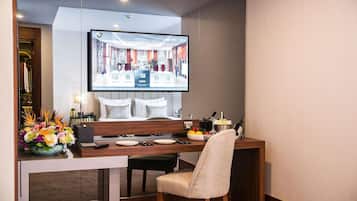 Een hotelkamer met een eethoek, een televisie waarop een hotelinterieur te zien is, een bloemstuk en een minibar.