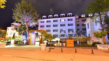 A hotel with multiple floors, a well-lit entrance, and a landscaped courtyard with potted plants and trees.