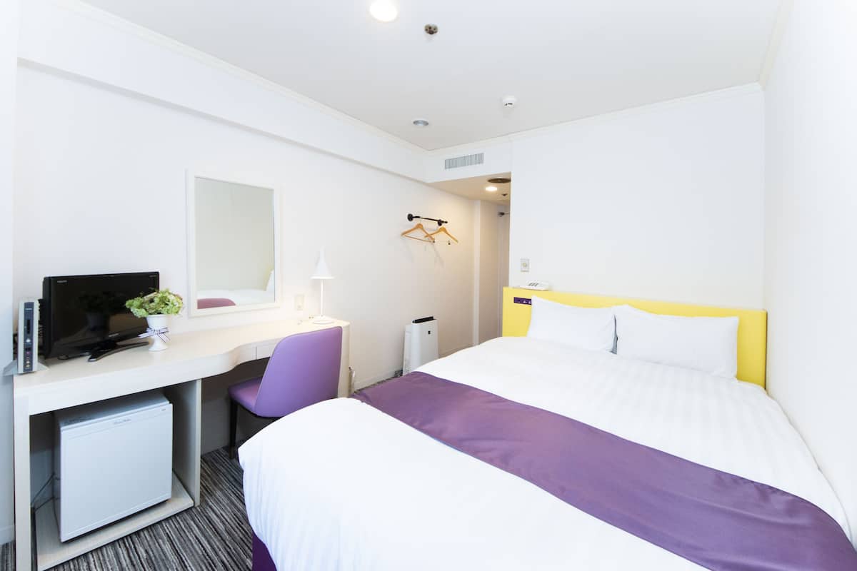 Habitación de hotel con cama, escritorio con computadora, silla, televisión y un refrigerador pequeño.