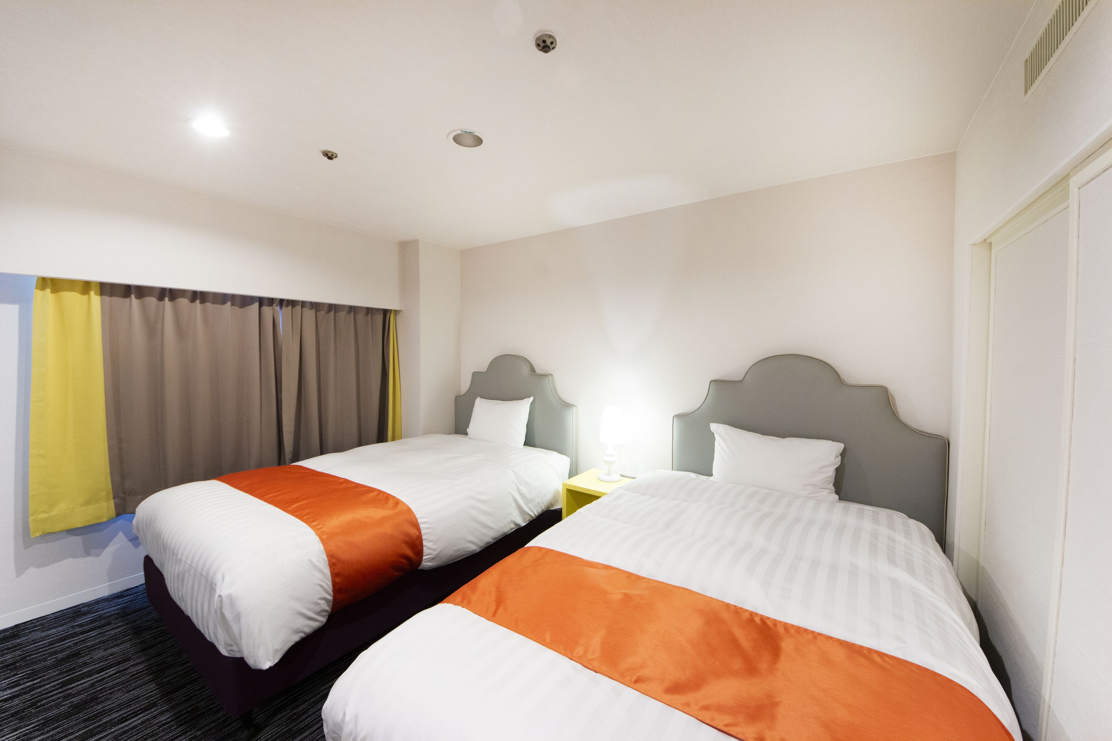 A hotel room with two beds, a nightstand, and a window with curtains.