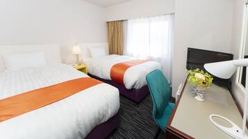 A hotel room with two beds, a desk with a lamp, a TV, and a window with curtains.