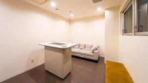 Una habitación pequeña con lavadora blanca, sofá color beige y ventana con persianas.