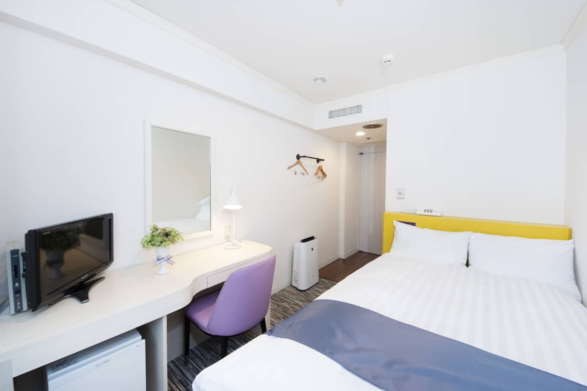 Habitación de hotel con cama, escritorio con computadora, una silla, televisión y una planta pequeña.