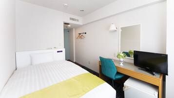 A hotel room with a bed, a desk with a computer, a chair, and a small refrigerator.