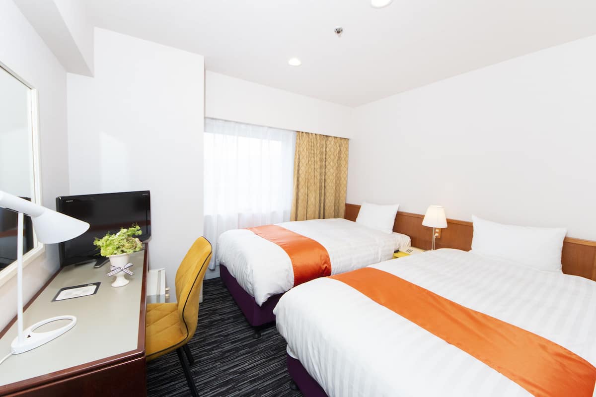 Habitación de hotel con dos camas, un escritorio con una computadora, una silla y una ventana con cortinas.