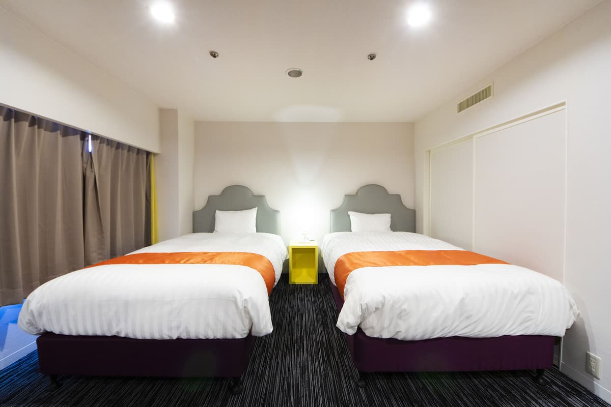 Habitación de hotel con dos camas, piso alfombrado y una ventana con cortinas.