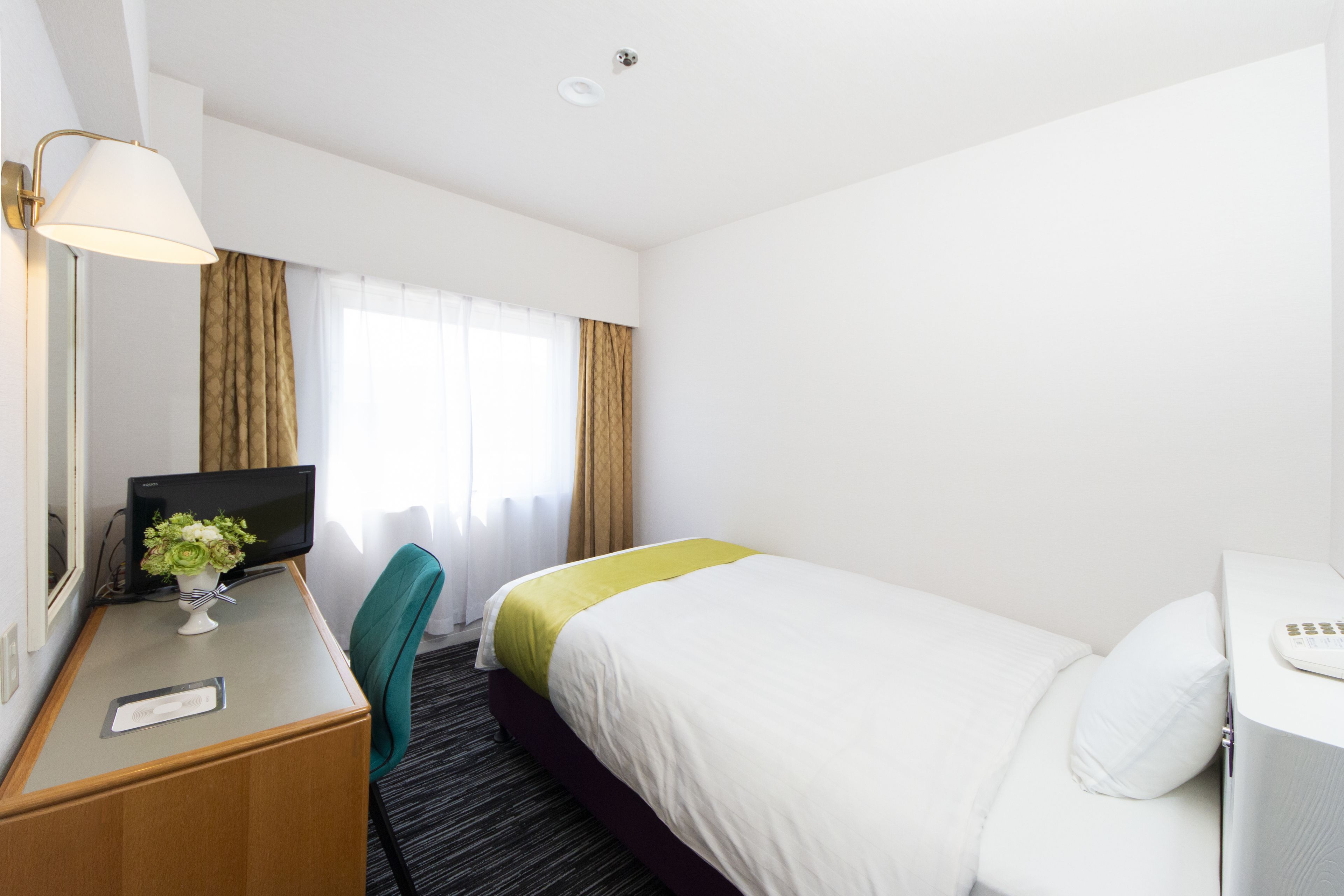 Ein Hotelzimmer mit einem Bett, einem Schreibtisch mit Computer, einem Sessel und einer Lampe.