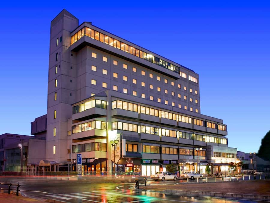 A multi-story hotel with a modern design, featuring a prominent corner entrance and multiple ground-level shops.