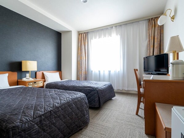 Habitació d'hotel amb dos llits, un escriptori i una televisió, i una cadira.