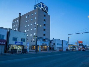 Un edificio de varios pisos con un letrero que indica un hotel. En la planta baja hay locales comerciales con señalización.