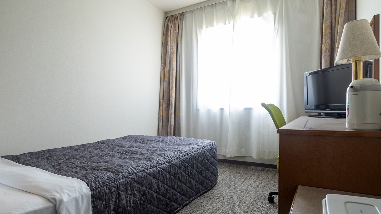 Hotellihuone, jossa on sänky, televisio, lamppu ja työpöytä.