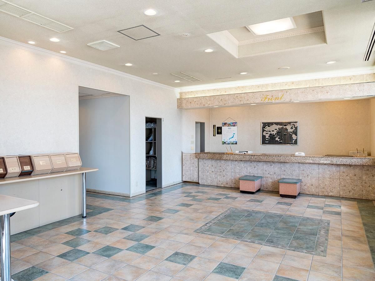 A hotel lobby with a reception desk, a waiting area with chairs, a counter, and a tiled floor.