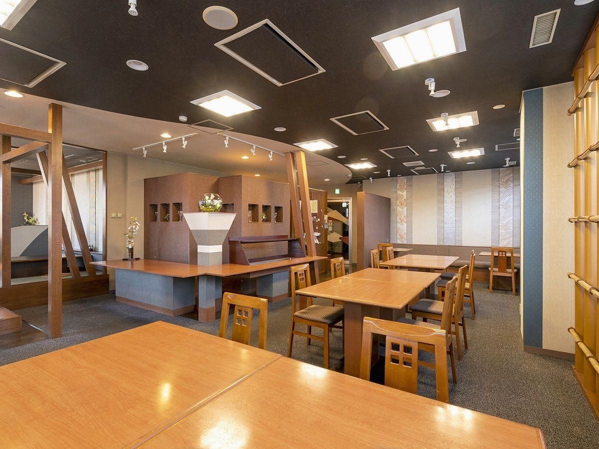 A restaurant interior with wooden tables and chairs, recessed ceiling lights, and a counter area.