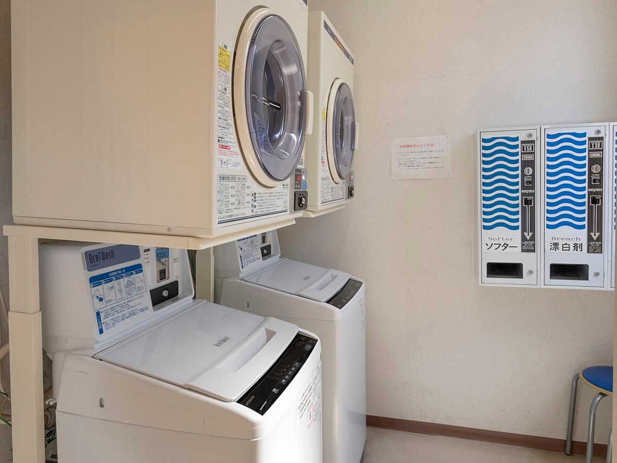 A laundry room with two washing machines and a dryer, a control panel with instructions, and a water meter.