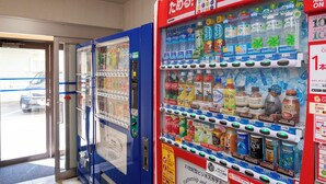 Vending machines with beverages and snacks, a glass door entrance, and a sign with Japanese text. - Hotel Paco Jr Kitami (Kitami)
