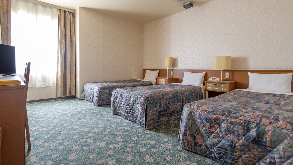 Hotellihuone, jossa on kaksi sänkyä, työpöytä, televisio ja lamppu.