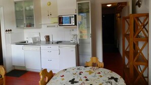 A compact kitchen with white appliances, a microwave, and a small refrigerator. There is a dining table with a floral tablecloth and wooden chairs. - 100m from ski slopes, parking, ski locker, 24m², Les 7 Laux (Le Pleynet)