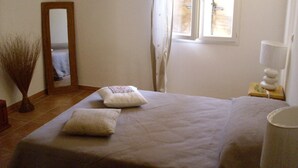 Ein Schlafzimmer mit einem großen Bett, einem Nachttisch mit Lampe, einem Spiegel und einem Fenster mit Vorhängen.