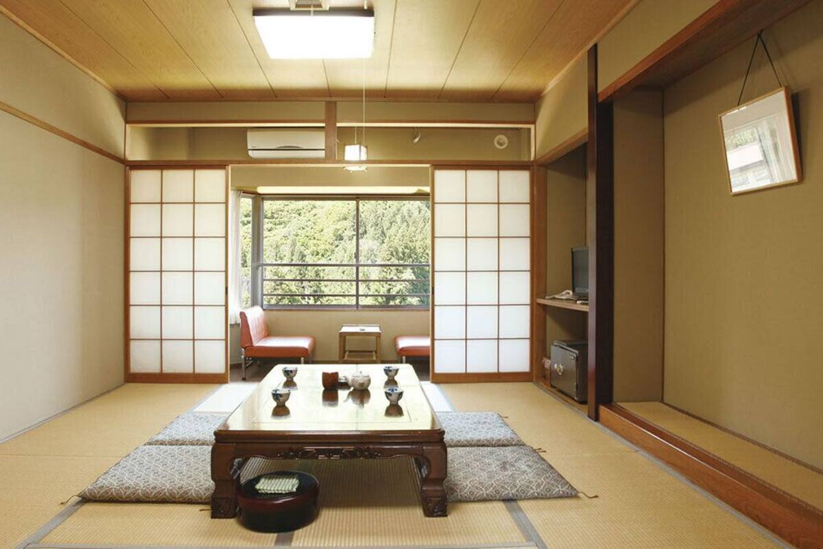 Una habitación japonesa tradicional con suelo de tatami, una mesita con juego de té, una puerta corredera y vistas a la vegetación exterior.