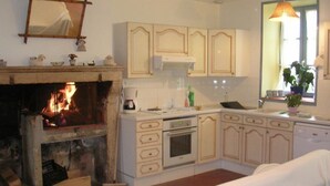 A kitchen with a fireplace, wooden cabinets, a coffee maker, and a window with a plant.