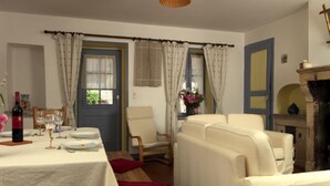 A room with a dining table set for two, a sofa, a chair, and a fireplace.
