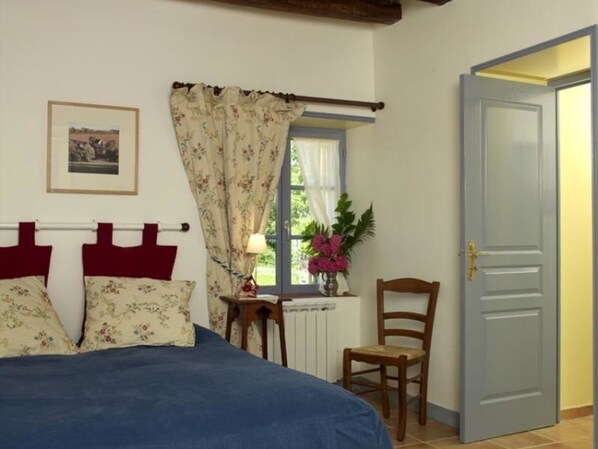 A bedroom with a bed, a chair, a window with curtains, a radiator, and a door.