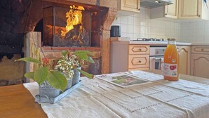A kitchen with a fireplace, wooden cabinets, a table with a placemat, a bottle of orange juice, and a magazine.
