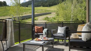 A balcony with outdoor seating, a table with food, and a view of a green landscape. - Outpost: One Town Hill 506 - Base of Snow King Mtn (Jackson)