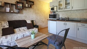 A compact living space with a sofa, a small table with a plant, a microwave, and a kitchenette with cabinets. - Cottage with pool and wifi in Ste Honorine (Sainte-Honorine-la-Guillaume)