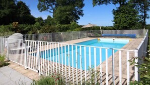 A rectangular outdoor swimming pool surrounded by a white fence, with a covered seating area and trees in the background. - Cottage with pool and wifi in Ste Honorine (Sainte-Honorine-la-Guillaume)