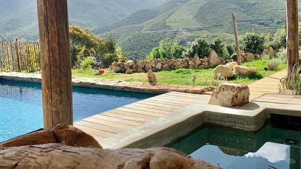Ein Poolbereich mit Holzterrasse, Kiesweg und Blick auf die Berge im Hintergrund.