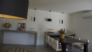 Ein moderner Essbereich mit einem langen Tisch, Stühlen, Pendelleuchten, einer Vase mit Blumen und einem Gemälde an der Wand.