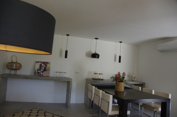 A modern dining area with a long table, chairs, pendant lights, a vase with flowers, and a painting on the wall. - Casa I&B (Peri)