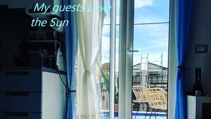 Ein Zimmer mit Blick auf einen Pool und Gartenmöbel, eine Tür mit Vorhängen und eine Tasche auf dem Boden.