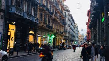 Una strada acciottolata fiancheggiata da edifici a più piani, alcuni con balconi e vetrine.