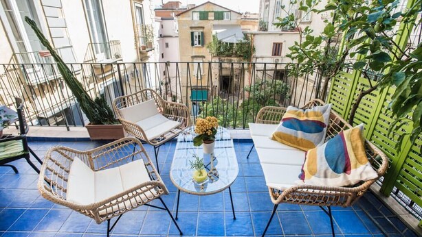 Ein Balkon mit Korbmöbeln, einem Glastisch und einem Blumentopf.