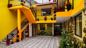 Un edificio a più livelli con pareti gialle, pavimento piastrellato e numerosi balconi ornati da piante in vaso.
