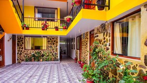 Un edificio a più piani con pareti esterne in giallo e pietra, un cortile piastrellato e piante in vaso.
