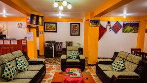 Una hall d'albergo con due divani, un tavolino, una televisione e opere d'arte alle pareti.