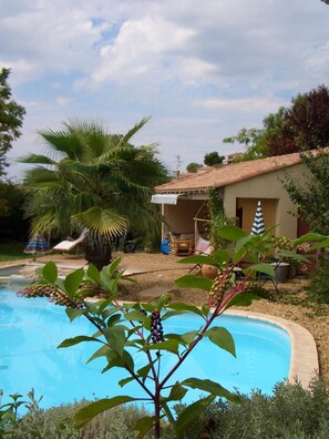 A swimming pool surrounded by greenery, a small house with a tiled roof, and a hammock. - Chambres d'hotes Beziers (Béziers)