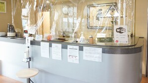 A hotel reception desk with a protective plastic cover, a digital clock, a coffee machine, and a sign indicating free Wi-Fi. - Hotel Stay in Sanno Plaza (Tsuruoka)